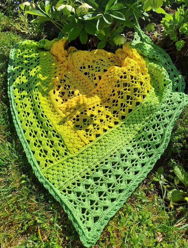 Yellow-to-green crocheted triangle shawl with openwork lace on grass