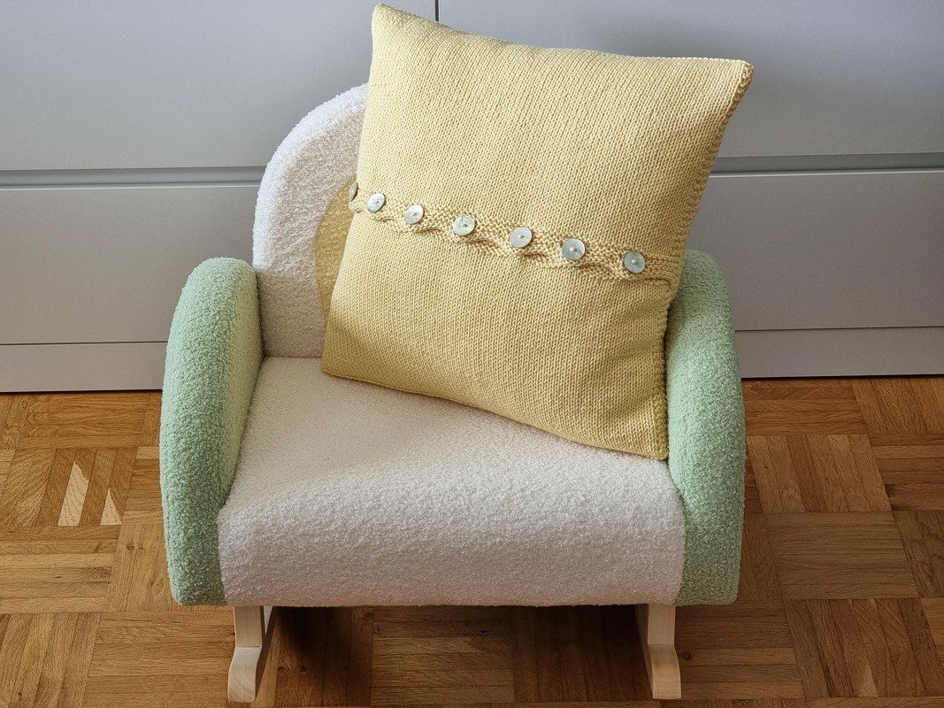 Gelbes gestricktes Kissen mit Reihe heller Knöpfe auf pastellfarbenem Sessel
