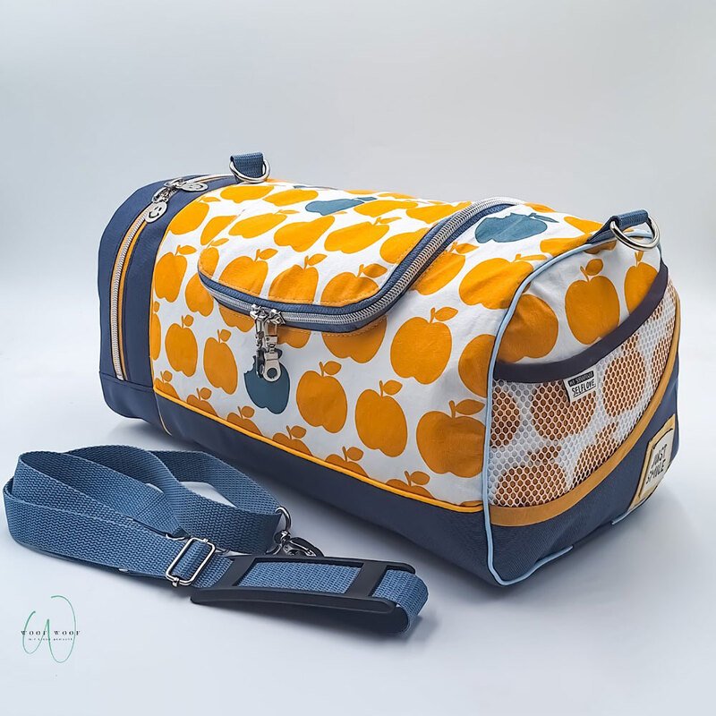 Sporttasche mit gelben Apfelmotiven auf weißem Stoff, marineblauem Unterteil und abnehmbarem Tragegurt.