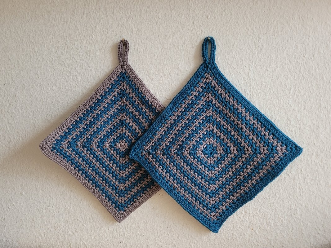 Zwei gehäkelte quadratische Topflappen in Blau und Grau mit Aufhängeschlaufen