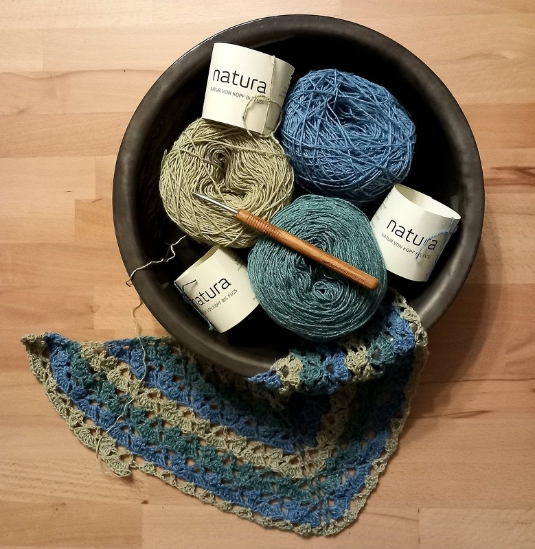 Schale mit Garnknäueln, Häkelnadel und halbfertigem blau-grünem Dreieckstuch