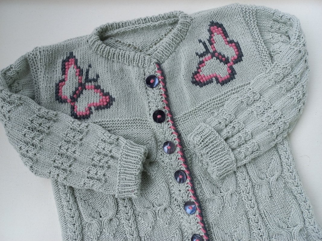 Hellgraue gestrickte Babyjacke mit rosa-schwarzen Schmetterlingen und dunklen Knöpfen