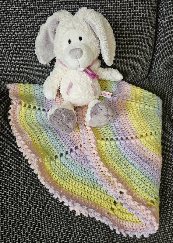 Nahaufnahme einer gehäkelten Decke in Pastellstreifen mit einem weißen Plüschhasen