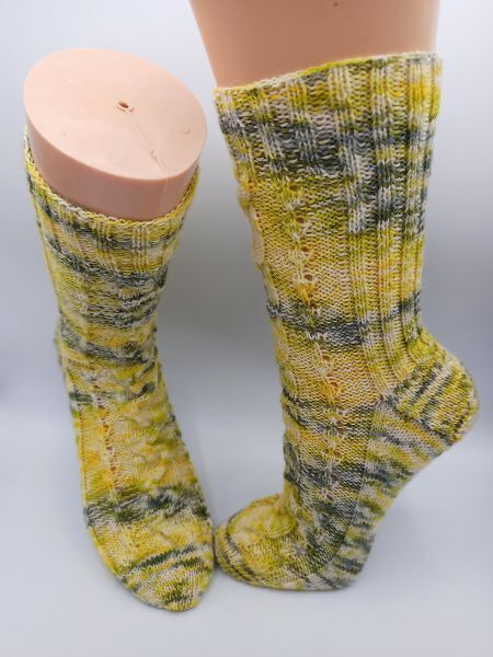 Stricksocken mit Rippenbündchen und Lochreihen in Gelb, Grün und Grau auf Sockenformen.