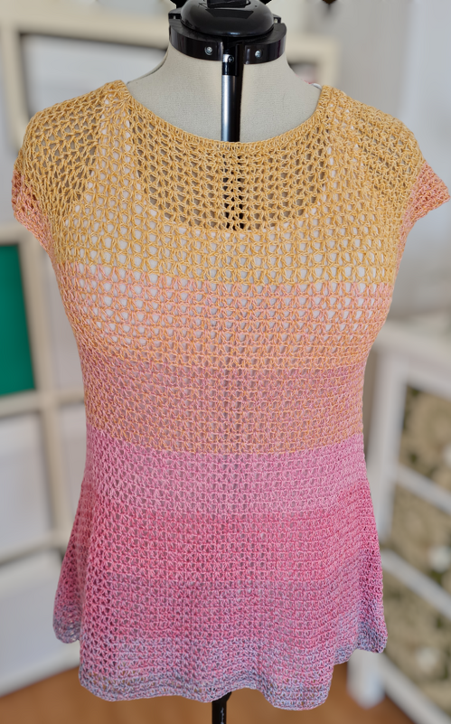 Gehäkeltes Damen-Top auf Schneiderpuppe mit offenem Maschenmuster und Farbverlauf von Gelb-Orange zu Pink.