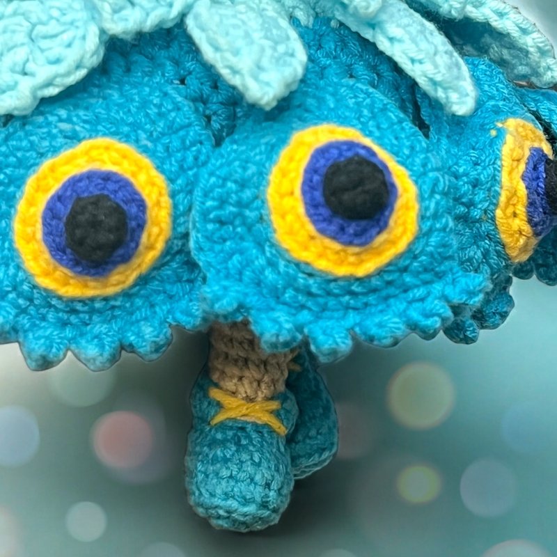 Close-up of teal crocheted amigurumi doll with yellow and purple circular appliqués and small laced shoes