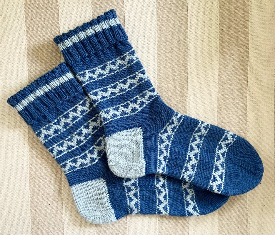 Gestricktes Paar Damensocken in Dunkelblau mit hellgrauen Zickzackstreifen auf gestreiftem Hintergrund.