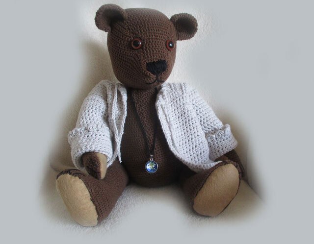 Gehäkelter brauner Teddybär mit hellgrauer Strickjacke und kleinem Globus-Anhänger