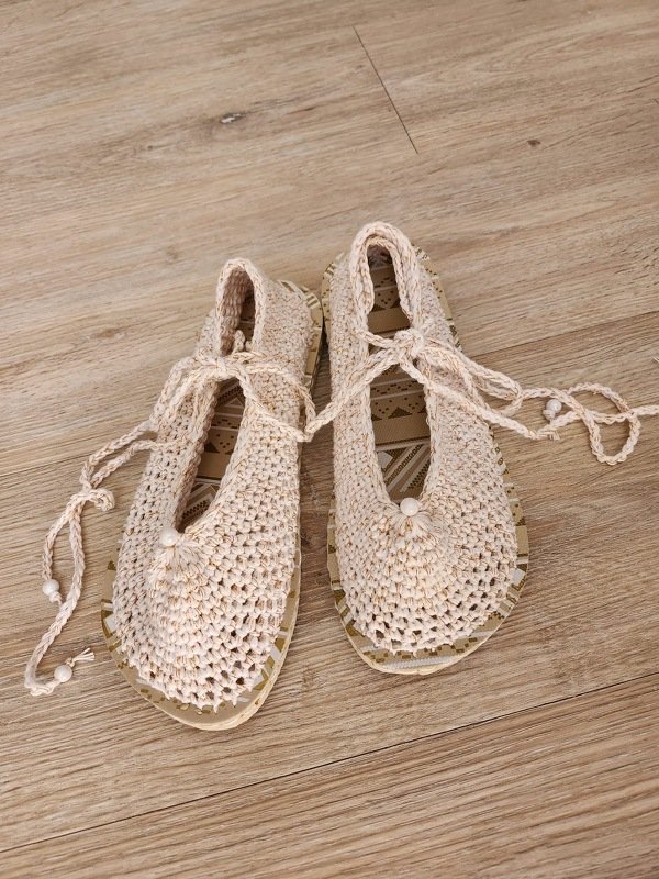 Paar gehäkelter naturweißer Ballerina-Schuhe mit Schnürbändern und Perlen auf Holzfußboden