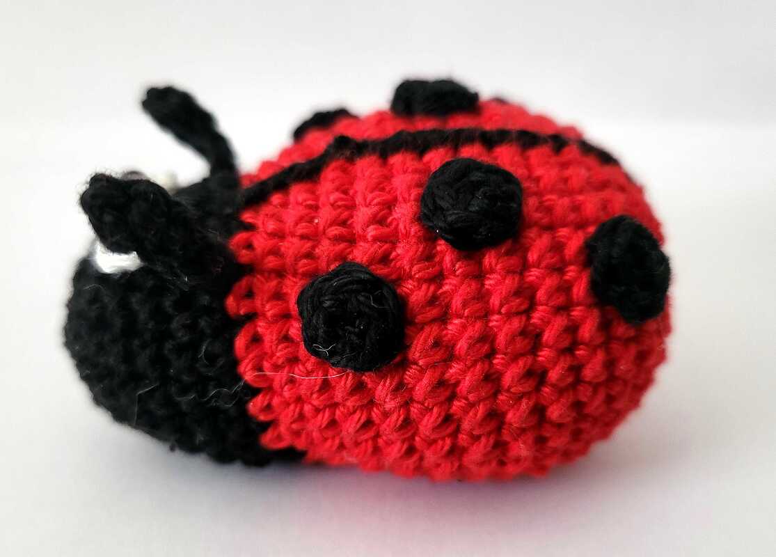 Nahaufnahme eines gehäkelten roten Marienkäfer-Amigurumi mit schwarzen Punkten