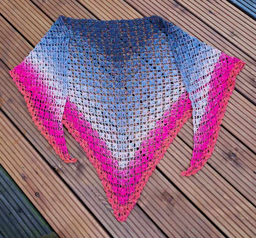 Gehäkeltes Dreieckstuch mit Farbverlauf (Blau–Weiß–Pink/Orange) auf Holzdielen