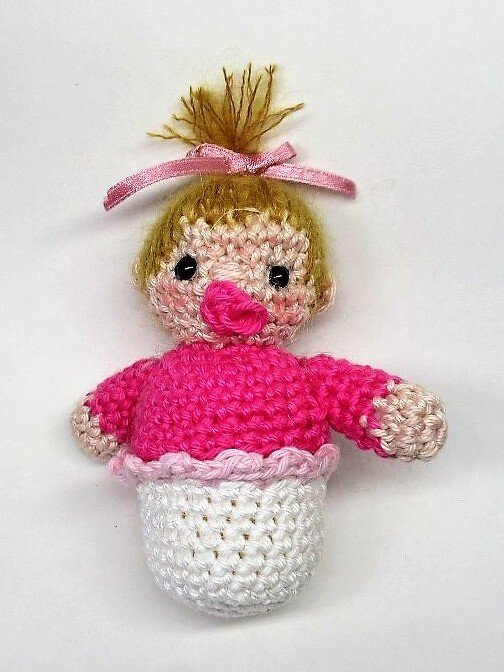 Gehäkeltes Amigurumi-Baby mit rosa Oberteil und weißem Unterteil, blondem Haarschopf, rosa Schleife und pinkem Schnuller