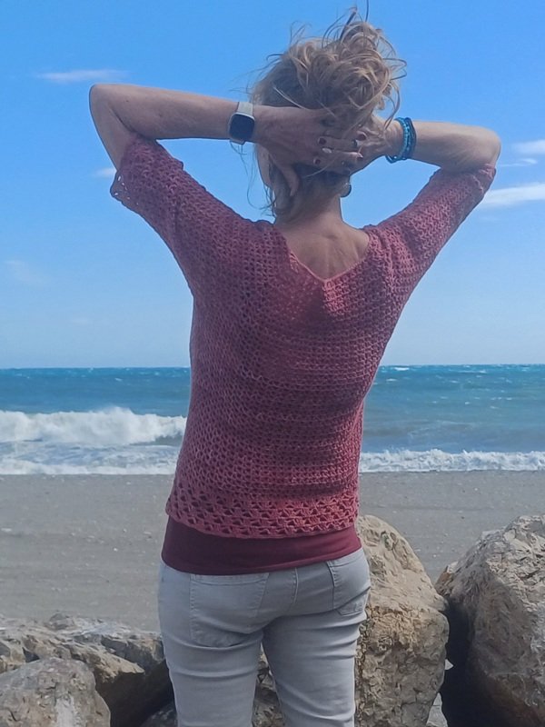 Rückansicht eines gehäkelten Kurzarm‑Shirts mit offenem Muster und Saumborte am Meer