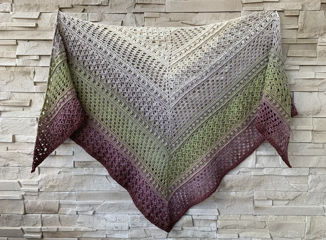 Triangle crochet shawl with cream-to-berry gradient and lacy stitch patterns pinned flat on a pale stone wall
