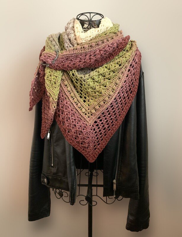 Multicolored crocheted triangle shawl with openwork and raised stitch textures draped over a dark jacket on a mannequin.