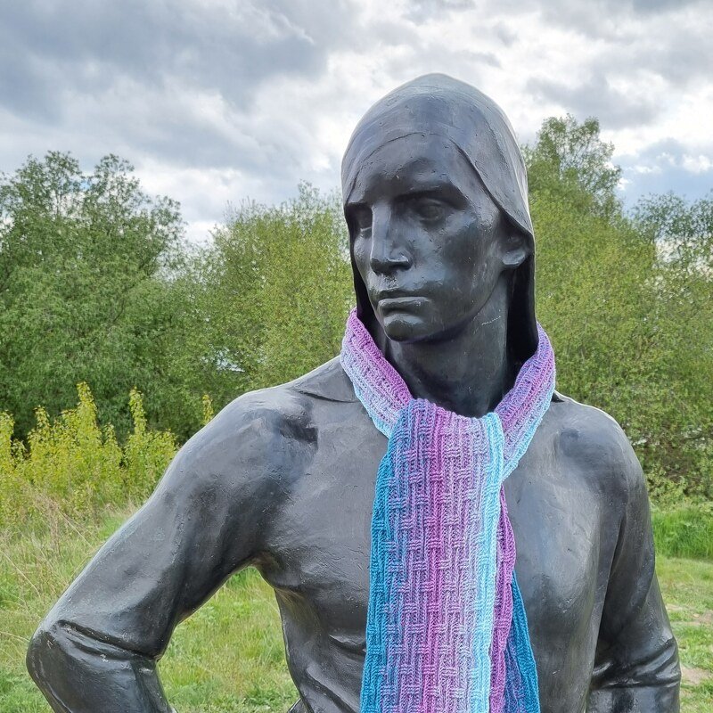 Gehäkelter schmaler Schal mit Reliefmuster und blau-lila Farbverlauf an einer Skulptur