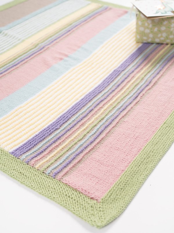 Gestrickte Babydecke mit Pastellstreifen und grünem Rand auf hellem Hintergrund.