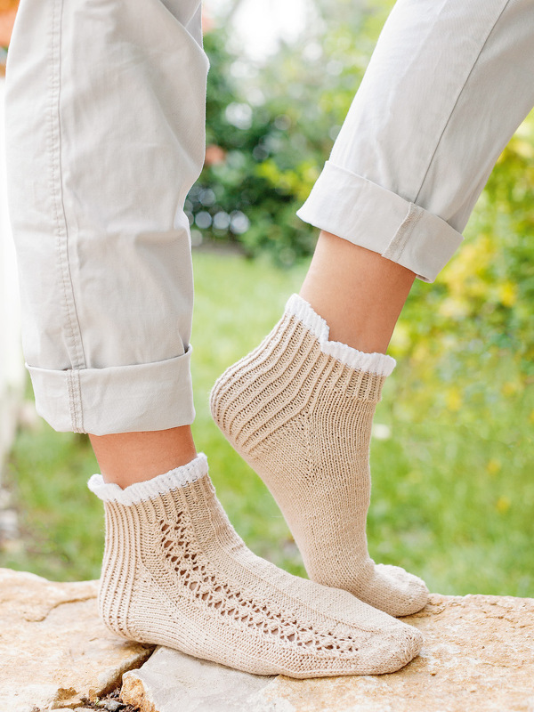 Beige gestrickte Knöchelsocken mit weißer Rüsche, Lochmuster und Rippbündchen an Damenbeinen