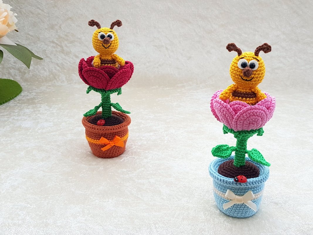 Zwei gehäkelte Bienen-Amigurumi in roten und rosa Blüten, in braunem und hellblauem Blumentopf mit Schleifen und Marienkäfer