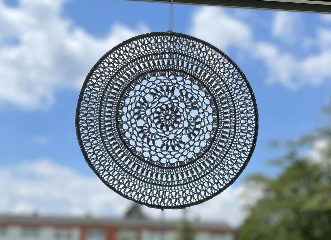Feines rundes Häkelmandala vor blauem Himmel mit lichtdurchlässigem Blumenmuster