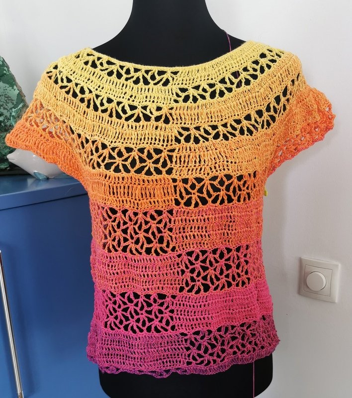 Gehäkeltes Damen‑Kurzarmshirt auf Schneiderpuppe in Gelb, Orange und Pink mit durchbrochenem Muster