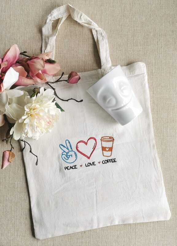 Helle Stofftasche mit besticktem Friedenszeichen, Herz, Kaffeebecher und dem Schriftzug 'Peace Love Coffee'.