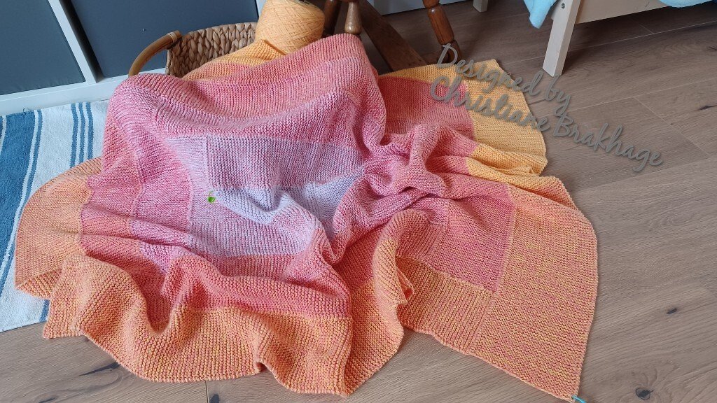 Mehrfarbige gestrickte Decke mit Farbverlauf in Gelb, Orange und Rosa auf Holzboden ausgebreitet