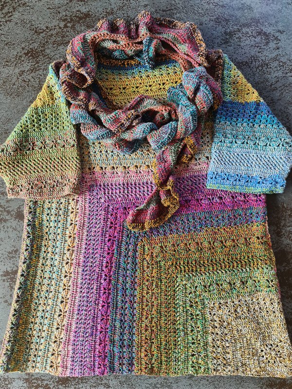 Bunt gehäkelte Tunika mit passendem Schal auf dunklem Untergrund ausgebreitet.