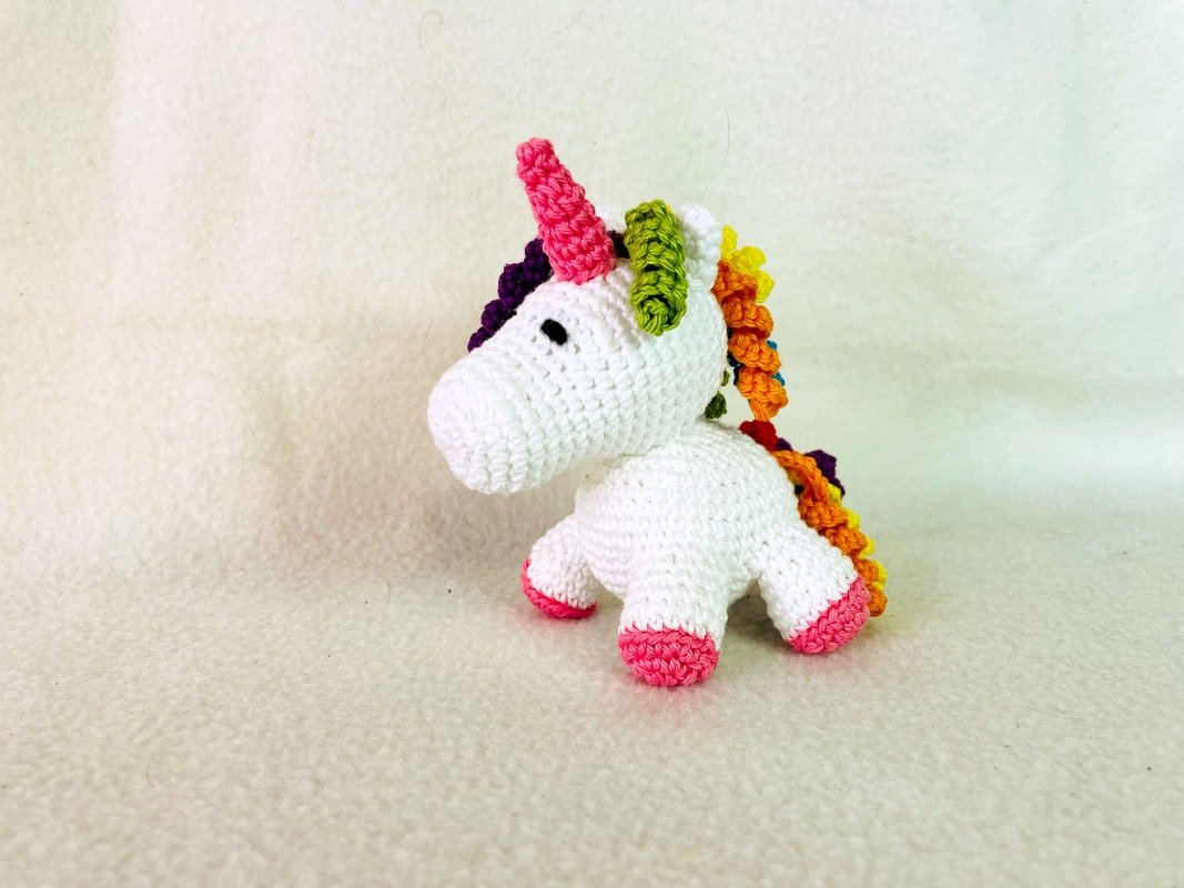 Weißes gehäkeltes Amigurumi-Einhorn mit Regenbogenmähne und rosa Hufen