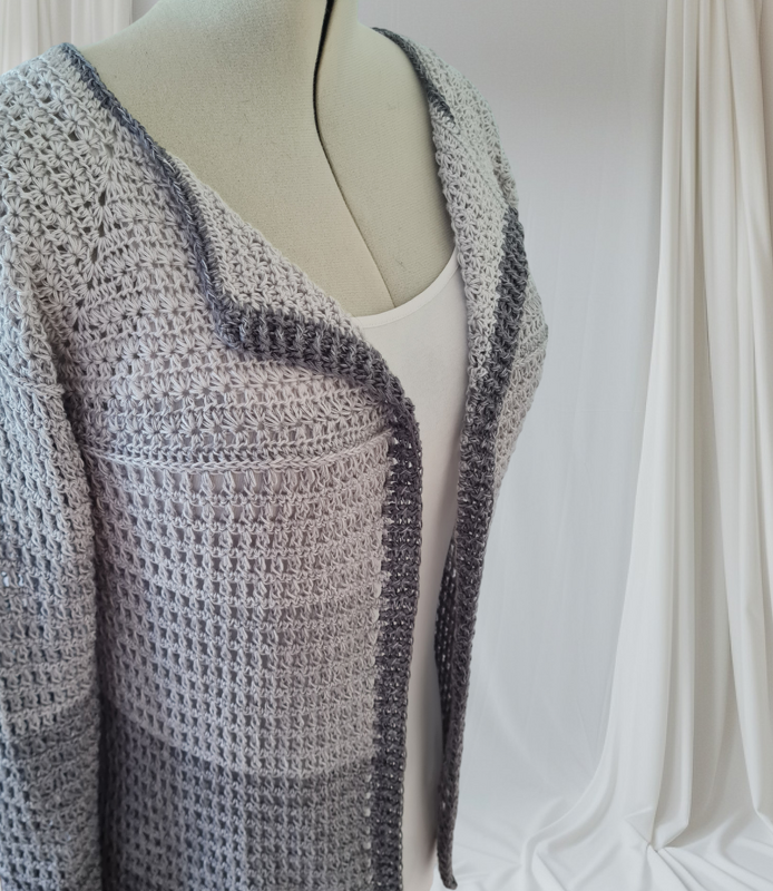Gehäkelte Damen-Cardigan in Grautönen auf Schneiderpuppe.