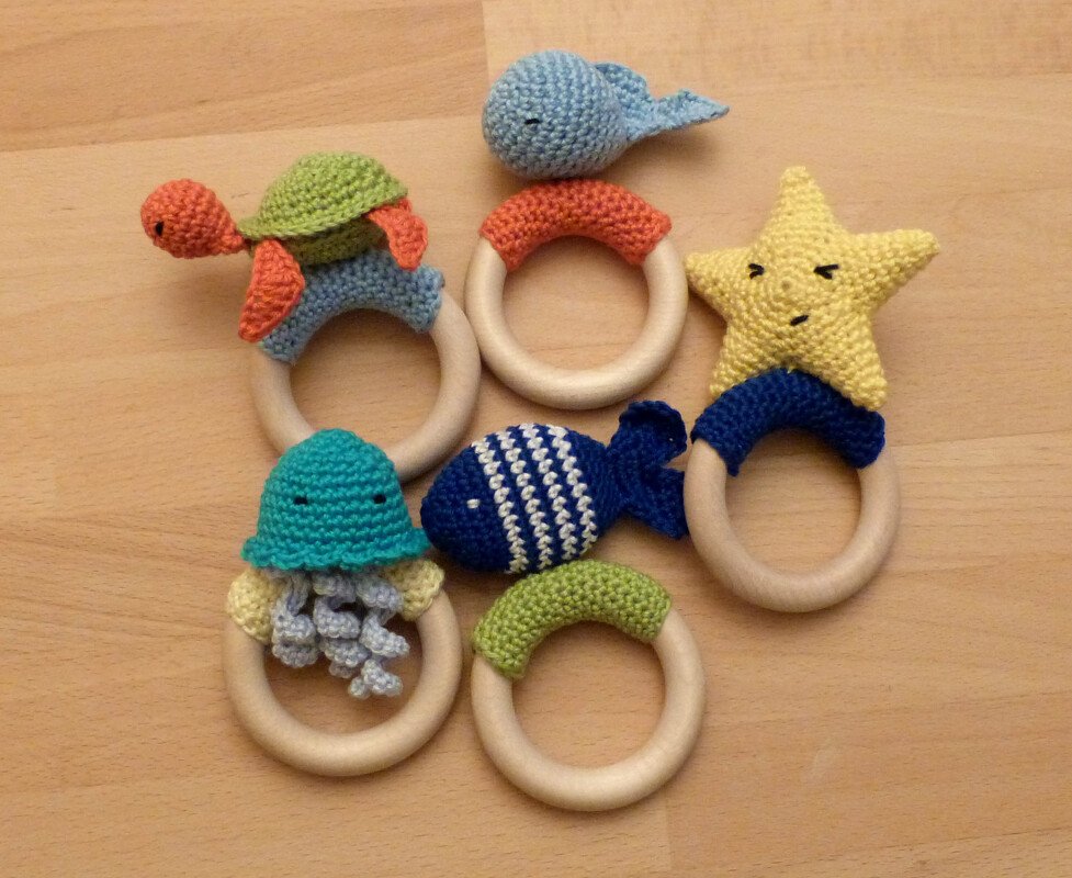 Sechs Holz-Greifringe mit gehäkelten Meeresmotiven: Schildkröte, Wal, gestreifter Fisch, Stern und Qualle.