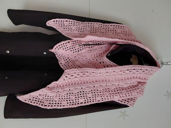 Rosa handgehäkelter Schal mit offenem Lochmuster, locker über dunkler Jacke drapiert.