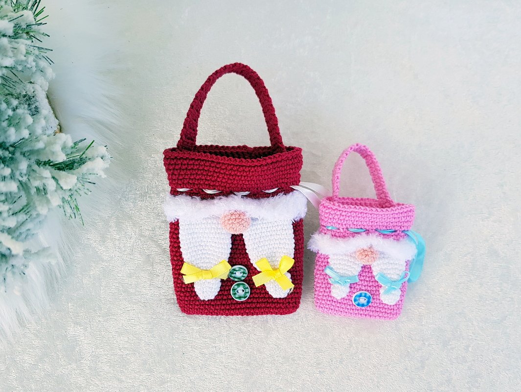 Zwei gehäkelte Wichtel-Taschen, eine rot und eine rosa, mit Griffen, weißen Bärten und Schleifen