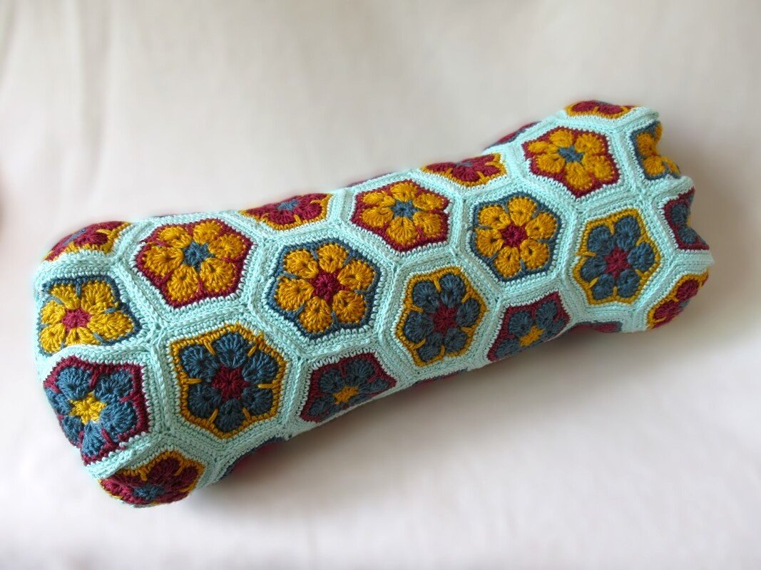 Gehäkelter Kissenbezug aus sechseckigen African‑Flower‑Motiven in Türkis, Senfgelb und Bordeaux