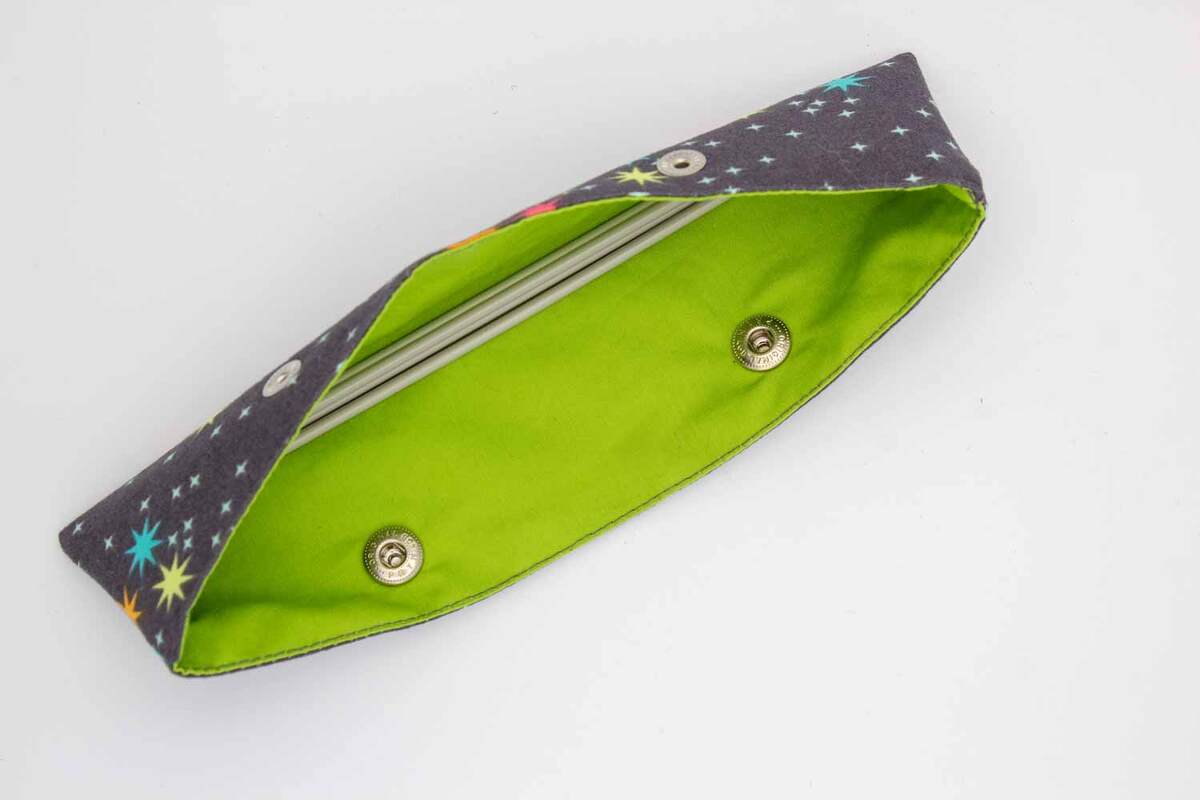 Geöffnetes Stoffetui mit buntem Sternenmuster außen und neongrünem Innenfutter, zwei Druckknöpfe sichtbar