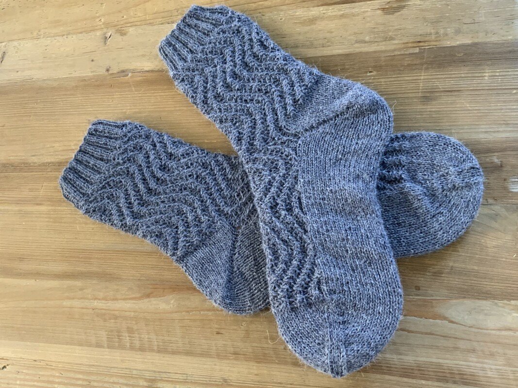 Detailaufnahme grauer Socken: geripptes Bündchen, Zickzack-Ajour und glatt gestrickte Ferse