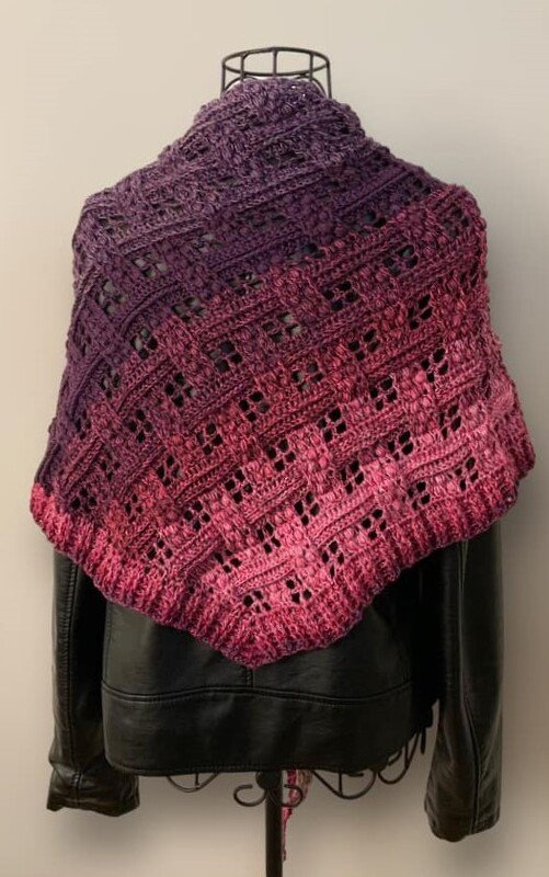 Crochet triangle shawl with purple-to-pink ombre and openwork lattice stitch, draped over a black jacket.
