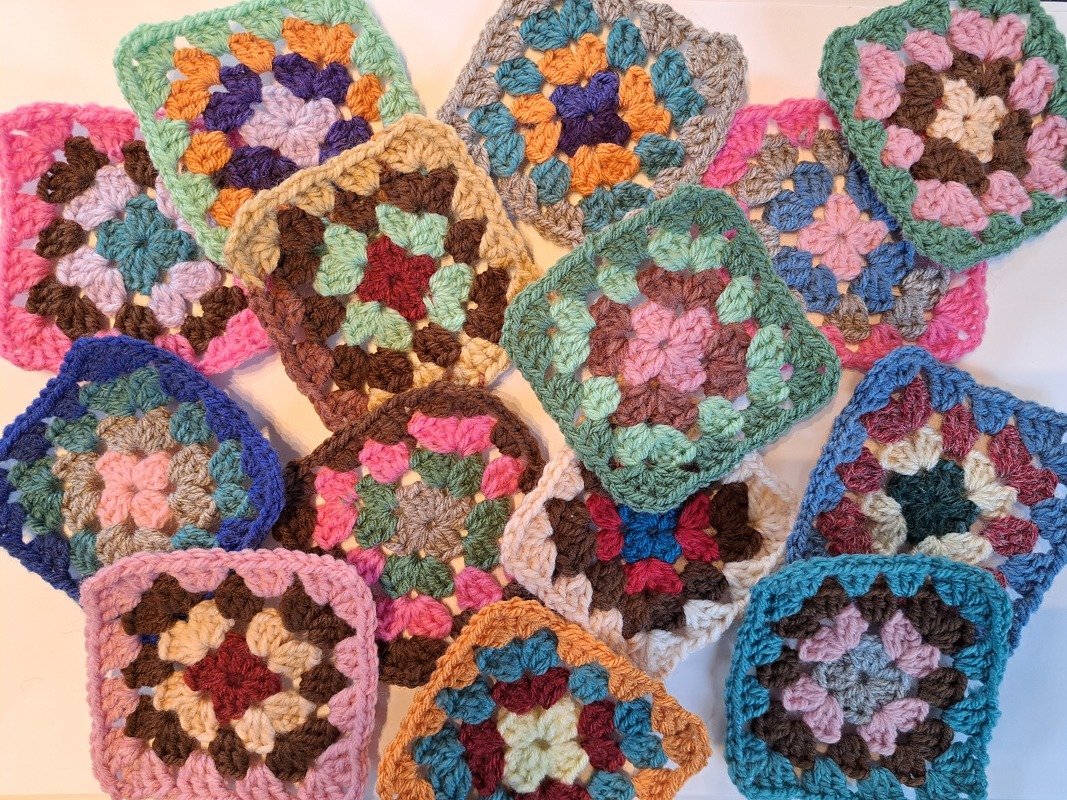 Mehrfarbige gehäkelte Quadrate (Granny Squares) in Pastell- und kräftigen Farben, locker angeordnet