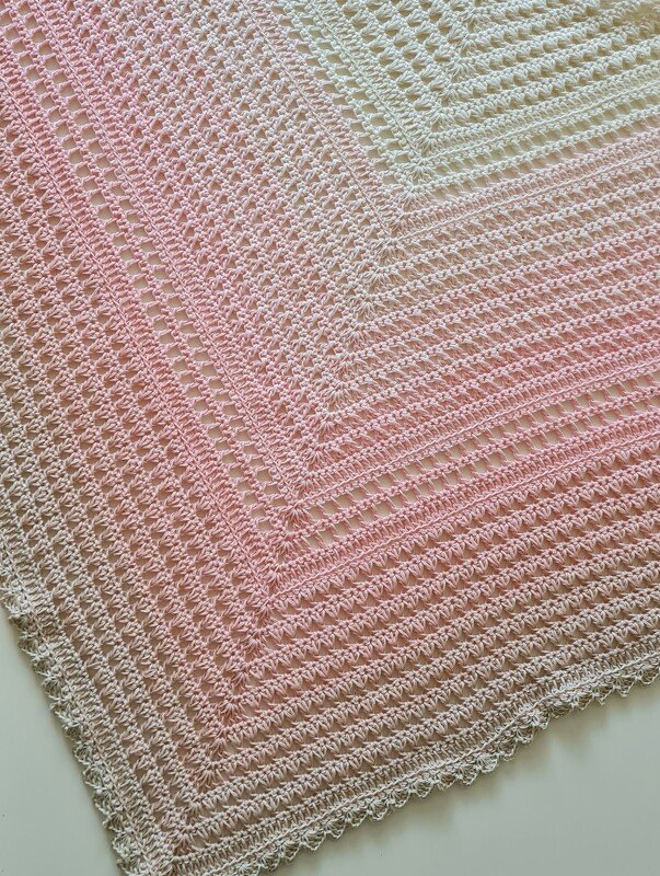 Detail eines gehäkelten Dreieckstuchs in Pastellrosa bis Creme mit Lochmuster und Muschelrand