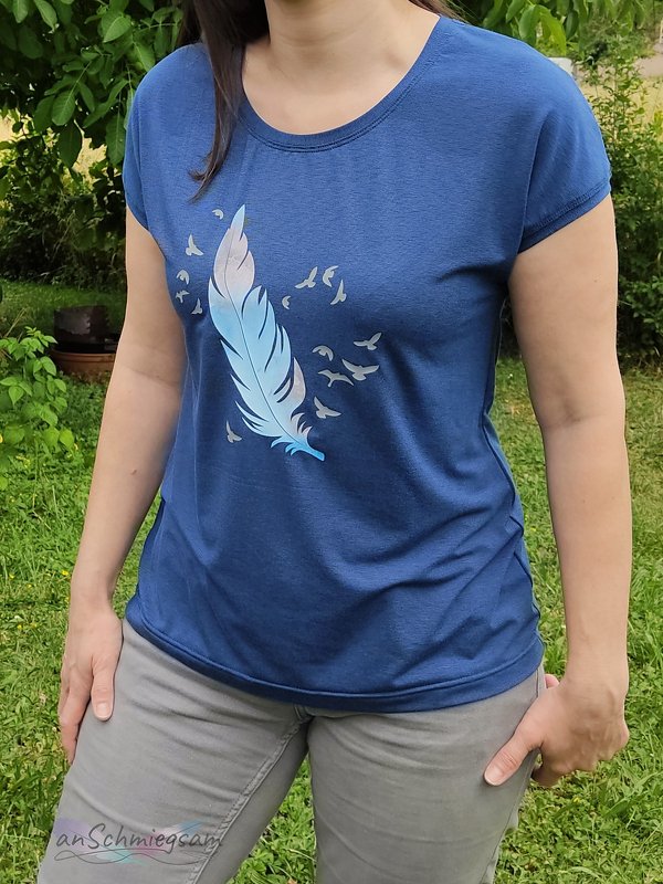 Person trägt dunkelblaues T-Shirt mit pastellfarbener Feder und kleinen Vogel-Silhouetten