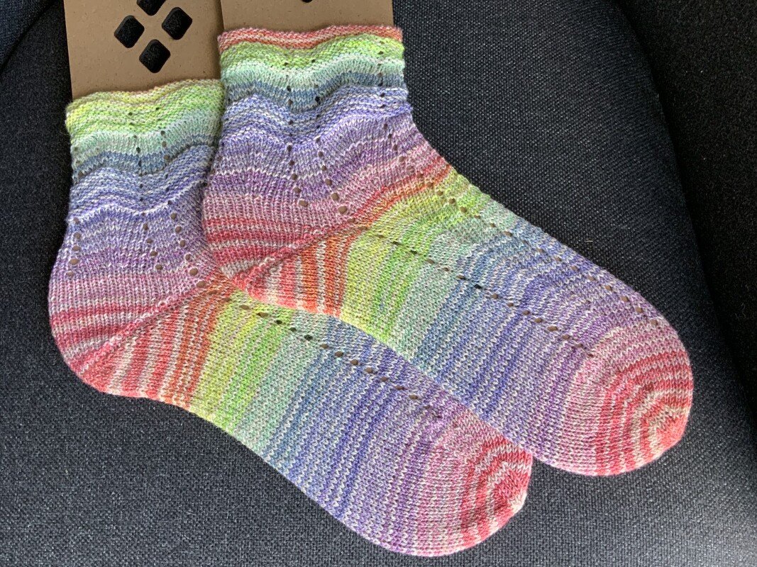 Paar handgestrickter Pastell-Socken mit Lochmuster auf dunklem Untergrund