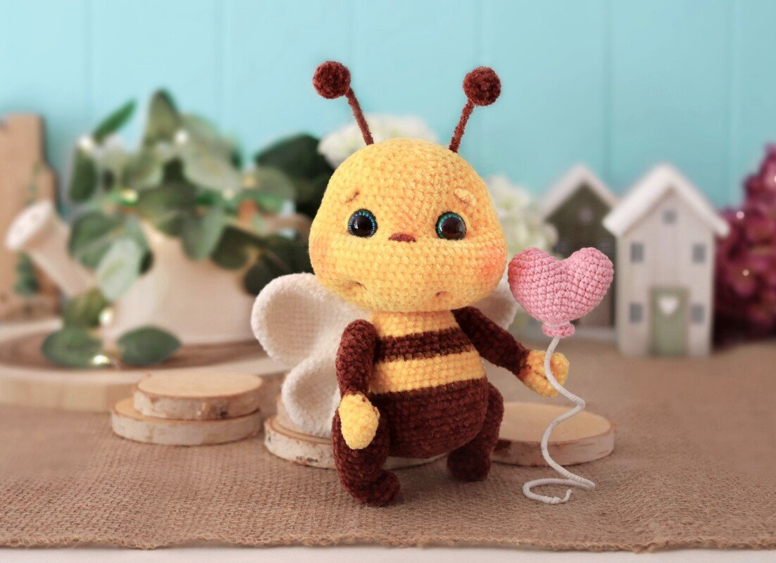 Gehäkelte gelb-braune Amigurumi-Biene hält einen rosa Herzballon