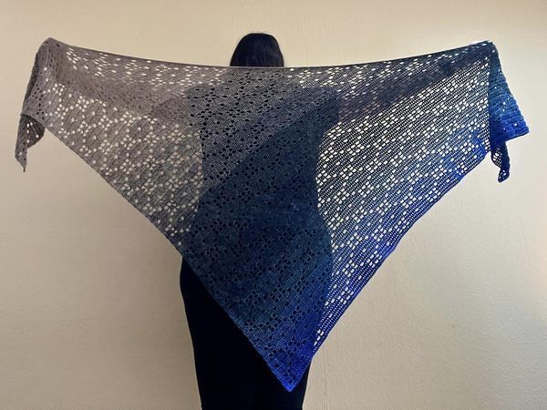 Person hält ein großes gehäkeltes Dreieckstuch mit Grau
Blauem Farbverlauf und Lochmuster
