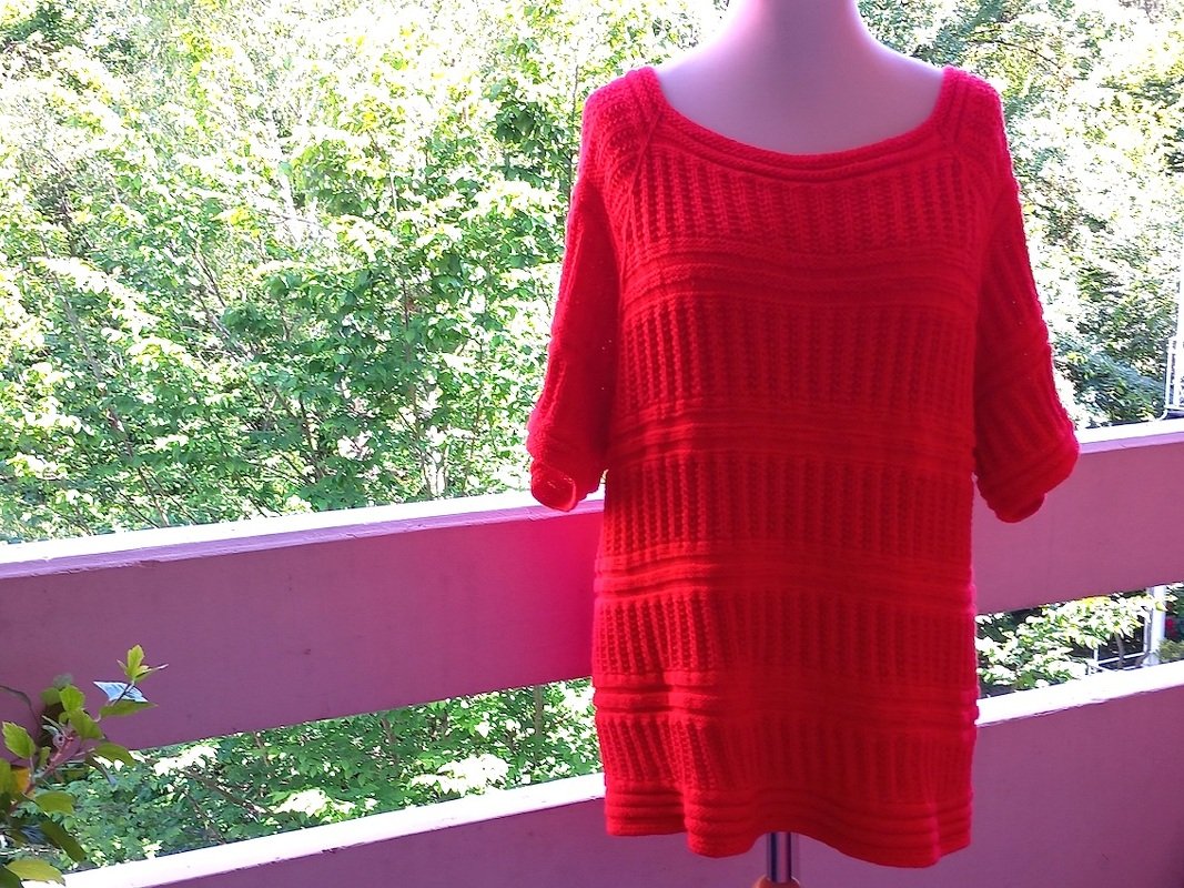 Roter gestrickter Damenpullover mit kurzen Ärmeln auf Schaufensterpuppe, Balkon mit Bäumen im Hintergrund
