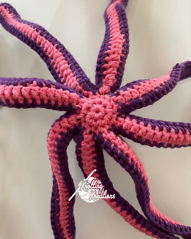 Top-down view of a crocheted octopus amigurumi with pink and purple striped tentacles.