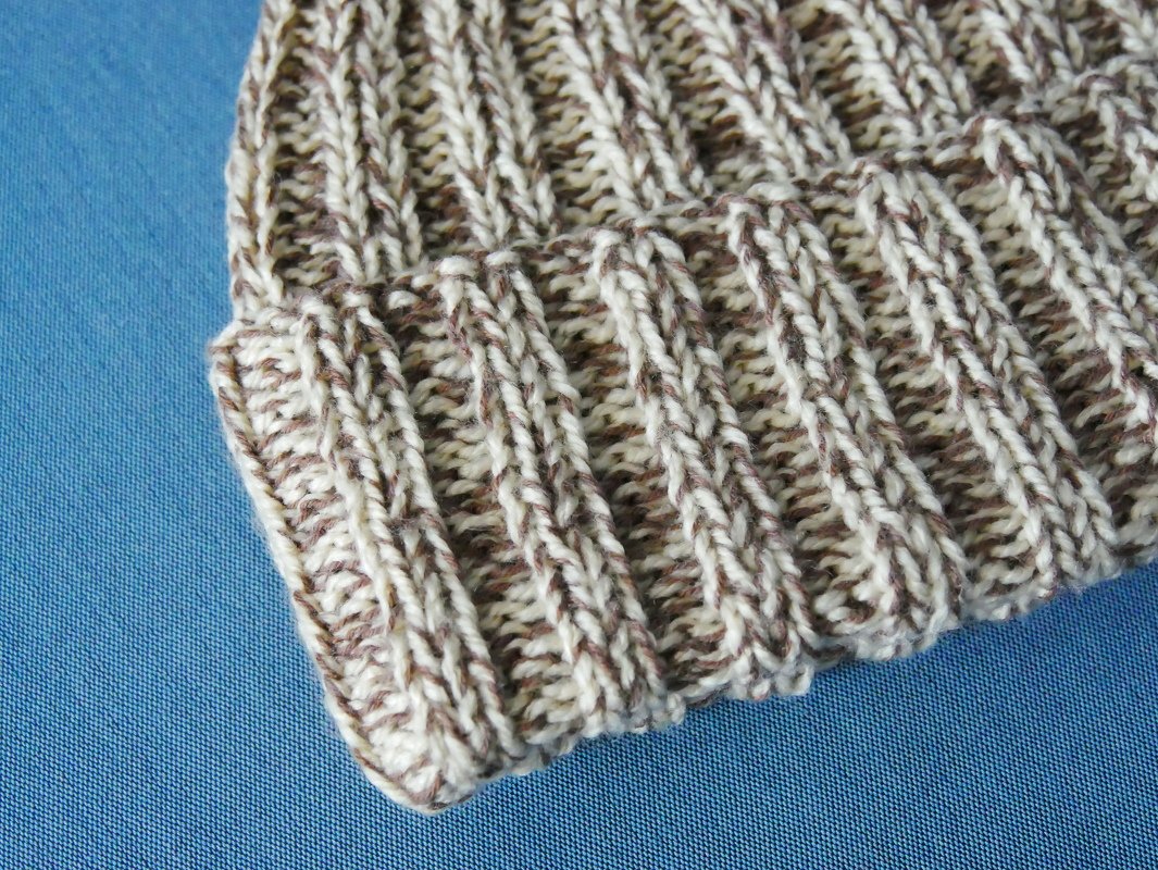 Strickmütze mit meliertem Garn in Braun und Beige im Rippenmuster auf blauem Hintergrund