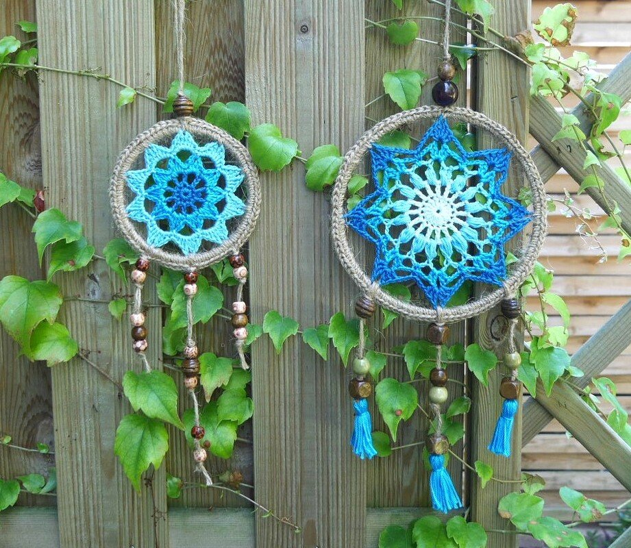 Zwei gehäkelte Traumfänger in Blau und Weiß mit Holzperlen an einem Holzzaun mit Efeu