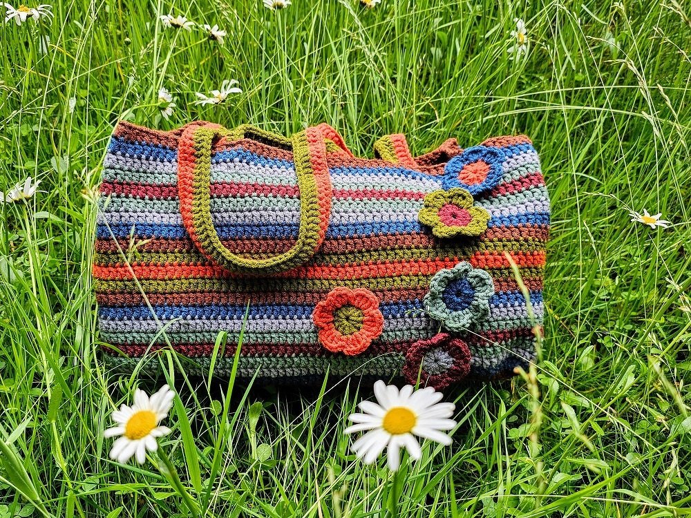 Gehäkelte, gestreifte Tasche mit Blumenapplikationen im grünen Gras