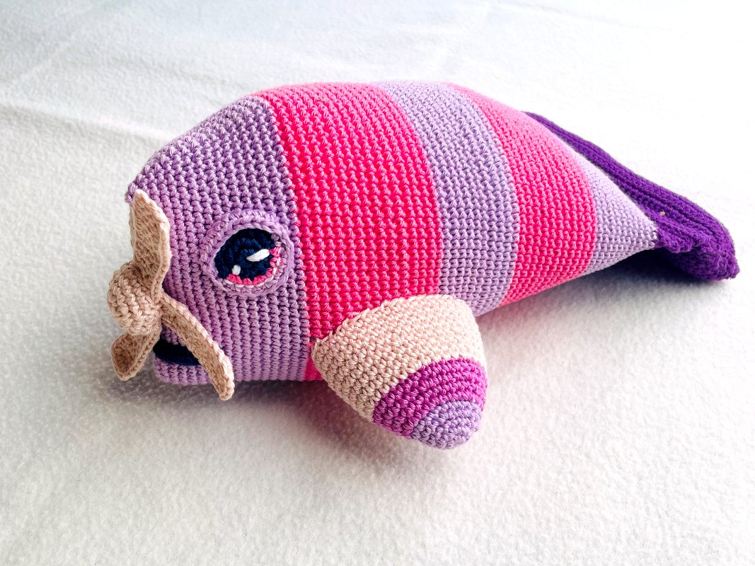Gehäkelter Amigurumi-Wal in gestreiften Lila- und Pinktönen mit kleinen Flossen auf hellem Untergrund.