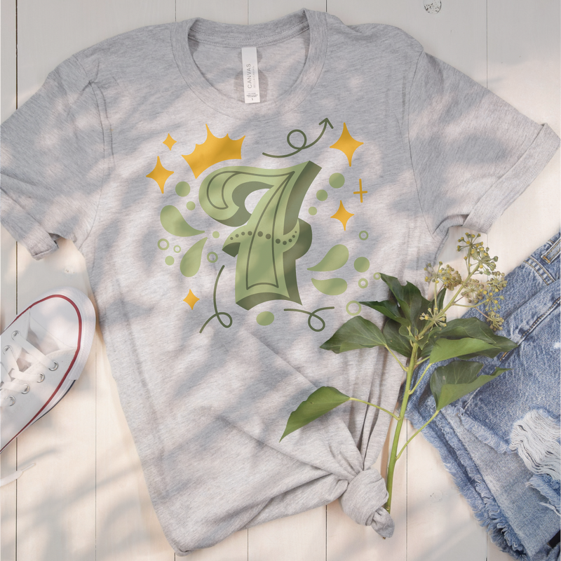 Grau meliertes T‑Shirt mit grünem Plot der Zahl 7, umgeben von goldgelben Sternen, einer Krone und floralen Elementen.